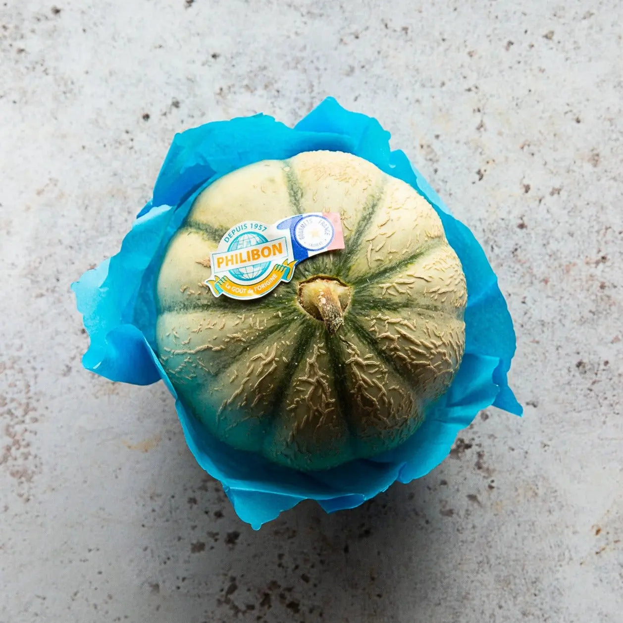 Charentais Melon | Premium French Cantaloupe by FINE & WILD wrapped in blue tissue, showcasing its netted rind and Philibon label.