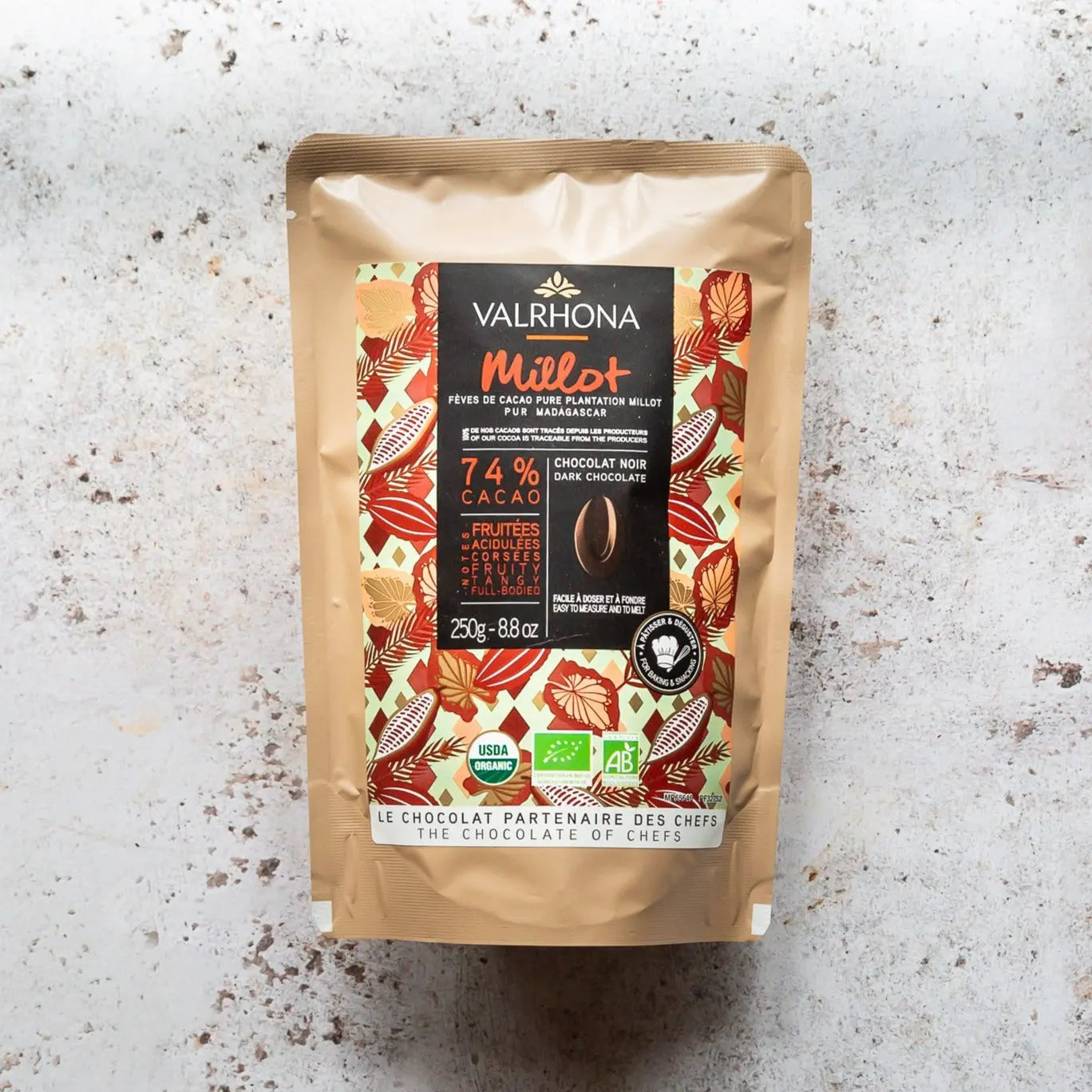 250g bag of Valrhona Millot Chocolate pieces on a grey background.