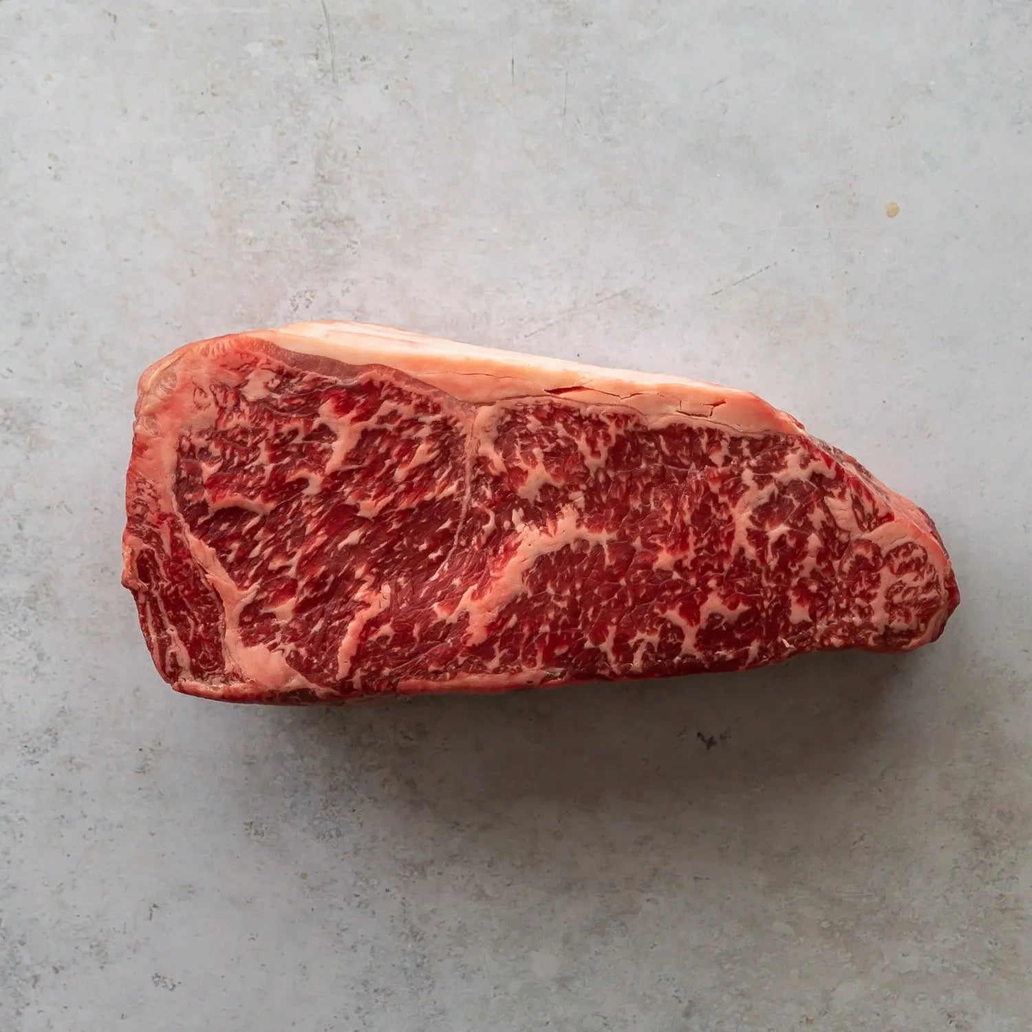 Picture of a highly marbled thick cut sirloin steak on a grey background.
