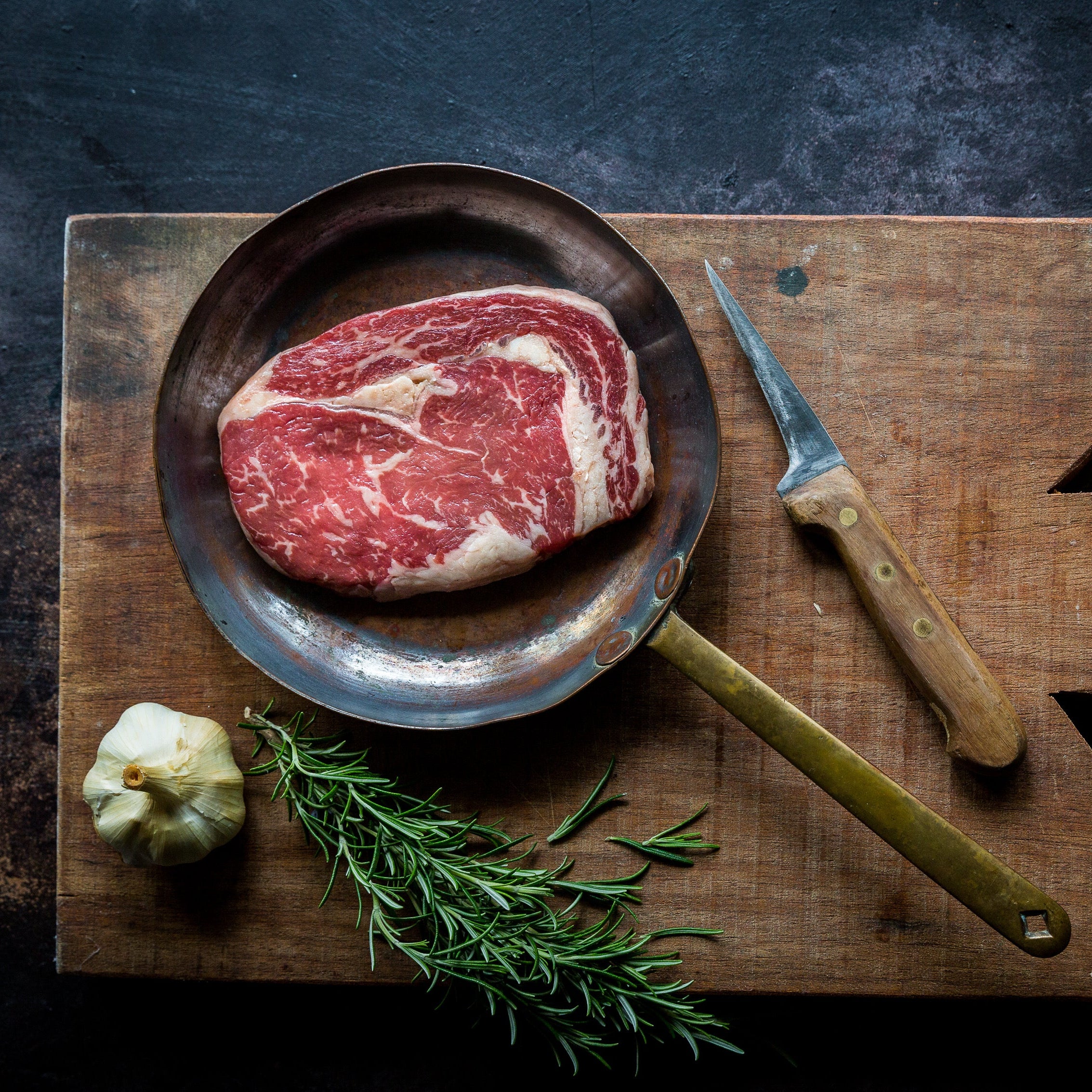 Raw beef ribeye steak on skillet with garlic and rosemary